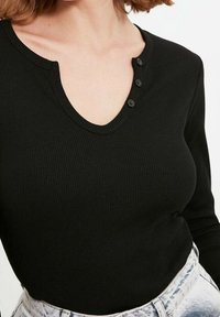 Svart ribbad långärmad topp med V-ringning och tre svarta knappar vid halsringningen, matchad med ljusa denimshorts.