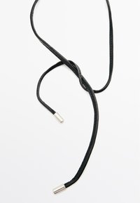 Corda in pelle nera con una superficie liscia, dotata di due estremità metalliche. La corda si attorciglia e si piega, mettendo in evidenza un design elegante.