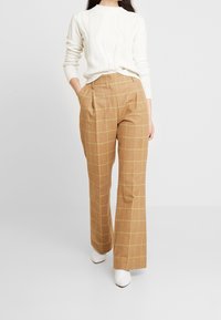 Cream knitted sweater with textured pattern paired with high-waisted brown plaid trousers featuring yellow grid lines and pleats.