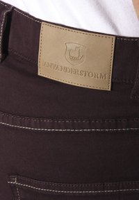 Dark purple fabric pants featuring a beige leather label with embossed logo, stitching details, and a back pocket visible.
