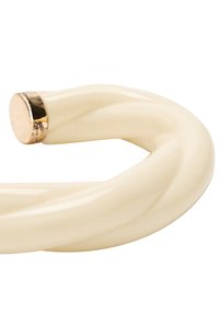 Zakładany, kremowy uchwyt o skręconym wzorze, z metalicznym, złotym akcentem na jednym końcu. Gładka tekstura, błyszczące wykończenie.