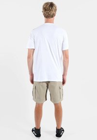 T-shirt blanc à manches courtes, short cargo beige et baskets noires. Design simple avec tissu lisse, coutures visibles et poches cargo.