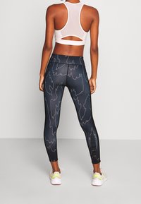 Leggings noirs ajustés avec un motif de lignes ondulées blanches, associés à un soutien-gorge de sport à dos nageur blanc avec un design à découpe.