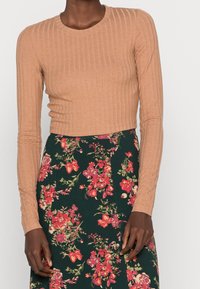 Top corto a maniche lunghe a coste color marrone chiaro abbinato a una gonna floreale verde con fiori rossi e gialli, creando un outfit a contrasto.