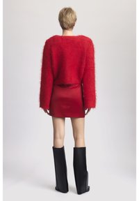 Pull court en peluche rouge, mini jupe rouge brillante et hautes bottes en cuir noires. Le pull a des manches larges et une texture douce.