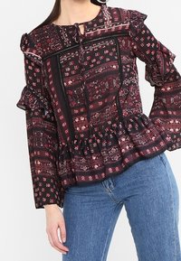 Blusa nera a maniche lunghe con sezioni floreali e a motivi rossi, maniche e orlo a balze, dotata di scollatura a chiave e fondo svasato.