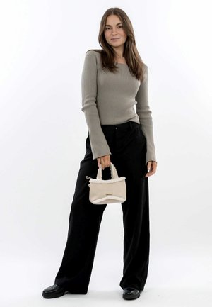 Grey ribbed long-sleeve top paired with loose black trousers. The model holds a small beige handbag with a soft white trim and gold hardware.