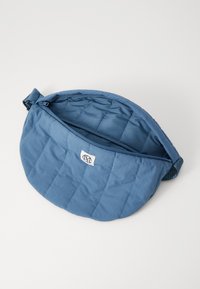 Borsa rotonda blu trapuntata con chiusura a zip, caratterizzata da un esterno in tessuto e un rivestimento interno morbido. Include un piccolo stemma con logo.