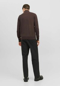 Pull en maille marron avec un col montant, associé à un pantalon noir ajusté et des chaussures noires. Texture lisse, design simple et couleurs neutres.