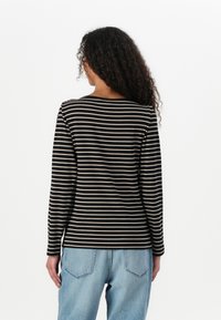 Langermet topp i svart og beige striper, med rund halsutskjæring og myk, elastisk stoff, kombinert med avslappet passform i lyseblå jeans.
