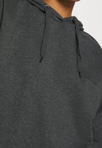 Mörkgrå hoodie med mjuk textur, dragsko-stängning och avslappnad passform. Visar minimala sömnadsdetaljer på tyget.