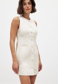 Robe sans manches ivoire à coupe droite, dotée de six boutons sur le devant, de deux poches latérales et d'une texture de tissu lisse.