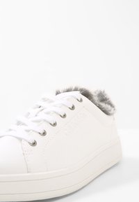 Sneaker bianca con fodera in finta pelliccia grigia al polsino, suola in gomma testurizzata e occhielli metallici per i lacci. Marchio impresso sul lato.