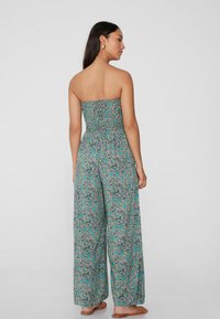 Mono sin tirantes, de flores en tonos verdes y azules, con un corpiño de fruncido, piernas anchas y una tela ligera y texturizada.