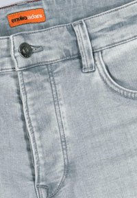 Light blue denim jeans featuring a classic five-pocket design, metal button closure, and orange brand label at the waistband.