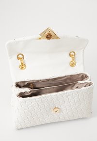 Vitt vävt läderclutch med guldkedjestraps, öppen klaff, beige tyginteriör och ett blixtlåsfack inuti.