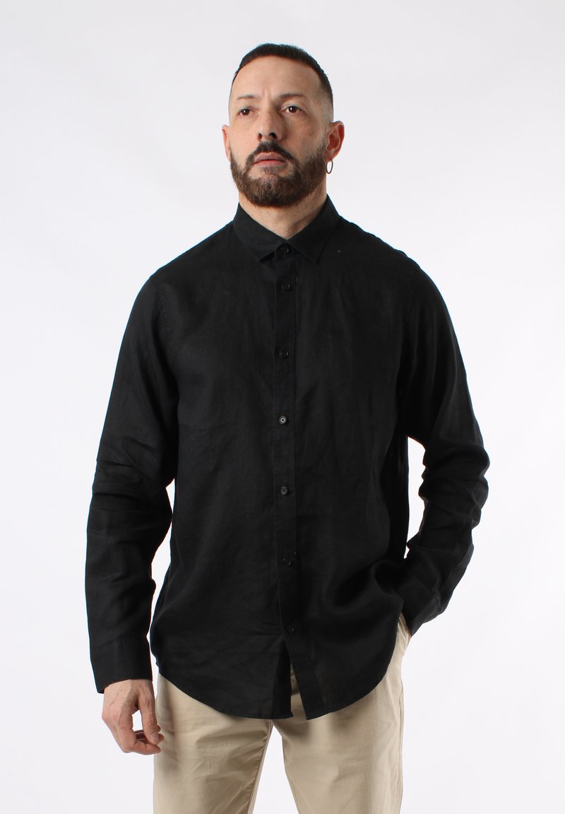 Camicia nera in lino con bottoni, maniche lunghe, colletto e bottoni anteriori. Indossata con pantaloni beige chiaro, con una texture liscia.