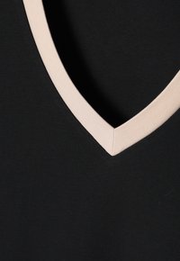 Black garment featuring a V-neck design with a contrasting beige collar. Smooth texture and clean edges on the neckline.