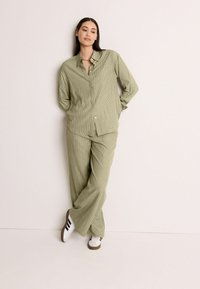 Chemise à rayures vert clair avec boutons, assortie à un pantalon large ; modèle portant des chaussures blanches avec des rayures noires.