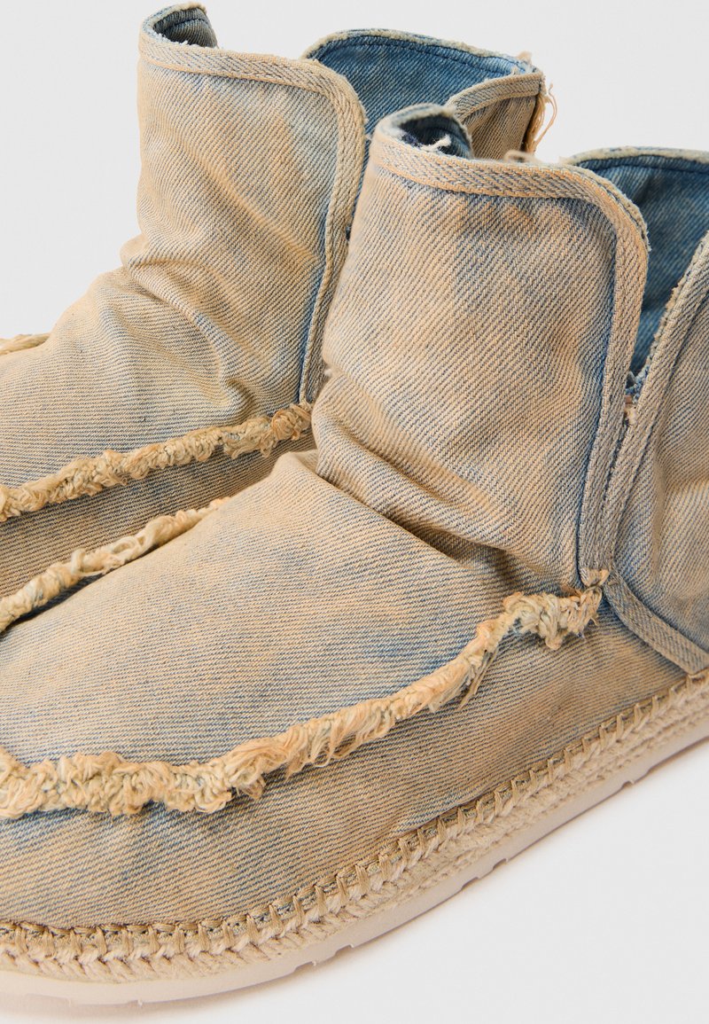 Stivali alla caviglia in denim con bordi sfibrati, texture morbida, colore azzurro chiaro e suola spessa in fibra naturale. Design leggero e flessibile.