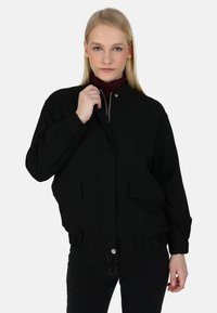 Giacca bomber nera con colletto alto, chiusura zip e tasche frontali. Presenta polsini elasticizzati e una vita arricciata. Tessuto dalla texture liscia.