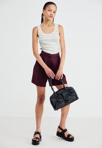 Black leather handbag with structured design, paired with a striped tank top and burgundy shorts, worn with chunky black sandals.