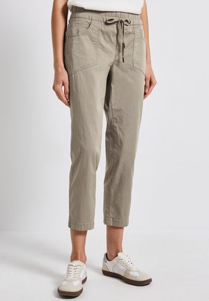 Pantaloni cropped color khaki chiaro realizzati in tessuto morbido, con vita elastica, coulisse regolabile e tasche laterali. Abbinati a sneakers bianche.