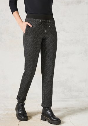 Pantalons à motifs noirs avec un design en losanges, taille élastique, poches latérales et coupe fuselée, associés à des bottes noires chunky.