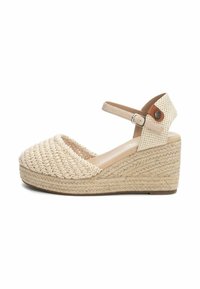 Sandale compensée tissée beige avec un dessus texturé, une bride de cheville réglable et une semelle en jute de style espadrille. Conception à bout fermé.