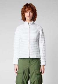 Giacca imbottita bianca con colletto alto e zip frontale. Presenta cuciture orizzontali e maniche lunghe, abbinata a pantaloni cargo verde oliva.