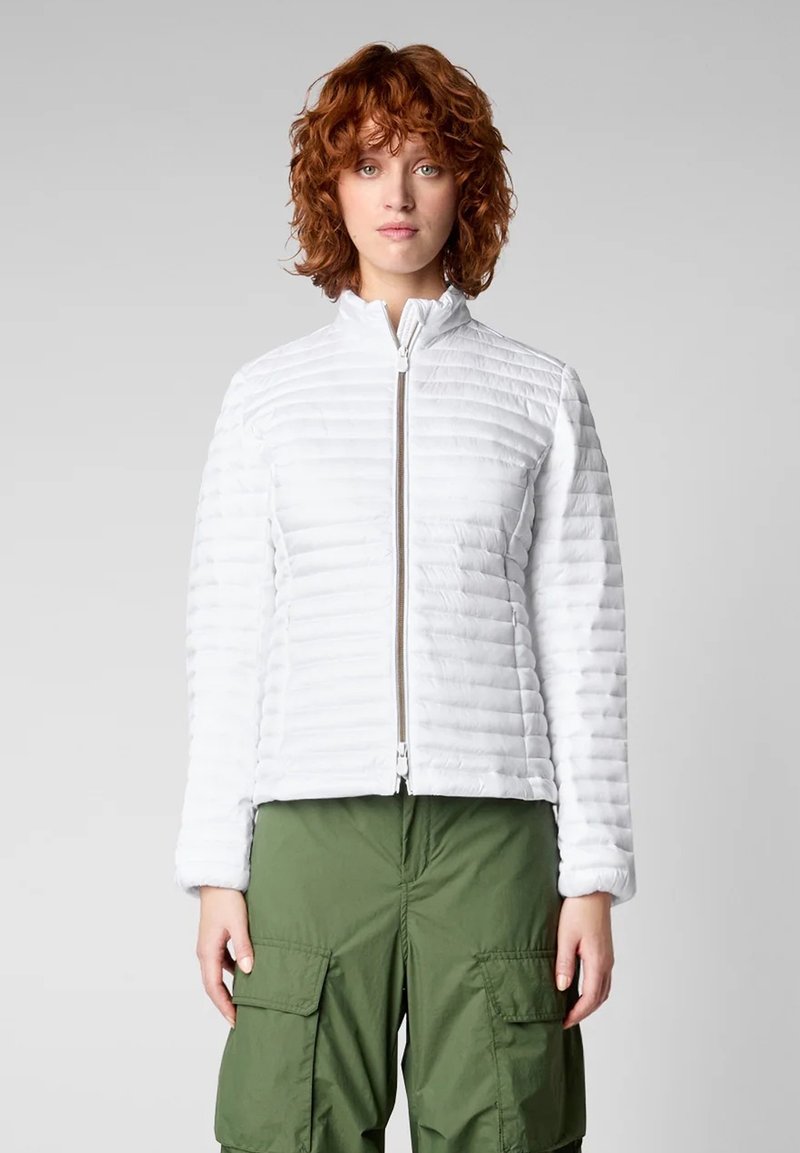 Giacca imbottita bianca con colletto alto e zip frontale. Presenta cuciture orizzontali e maniche lunghe, abbinata a pantaloni cargo verde oliva.