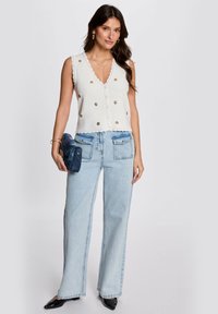 Top bianco senza maniche con bordi scallop e ricami floreali, abbinato a jeans a gamba larga azzurri e una borsa blu scura.