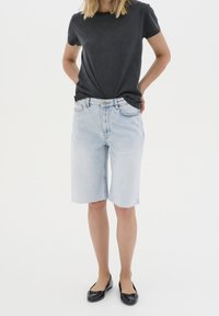 Svetle modré džíny šortky se rovnoměrným střihem a roztrhaným lemem, spárované s černým topem s krátkým rukávem a černými balerínami.