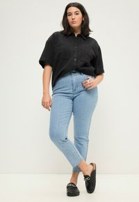 Camisa negra de botones de manga corta con dos bolsillos en el pecho, jeans de tiro alto a rayas azul claro y mocasines negros sin cordones con detalles de cadena.