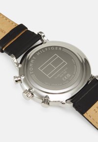 Fondo de acero inoxidable para reloj con logotipo grabado, dos botones pulsadores y correa de cuero negro. Resistente al agua hasta 5 bares.