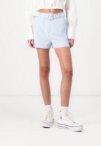 Pantaloncini personalizzati blu chiaro con vita cinturata e tasche laterali, abbinati a sneakers alte bianche e calzini alla caviglia.