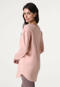 Top rosa chiaro a maniche lunghe con vestibilità rilassata, caratterizzato da una scollatura arrotondata, spacchi laterali all'orlo e una texture liscia. Abbinato a leggings marroni.