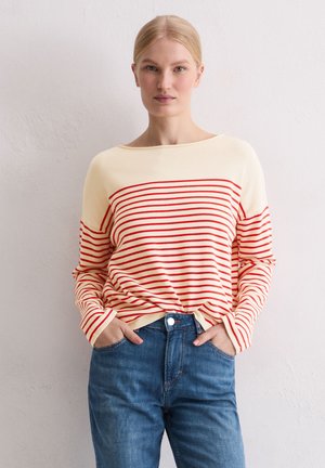 Maglione a righe rosse e crema in maglia, con scollo ampio, maniche lunghe e orlo a costine, indossato sopra jeans blu a vita alta.