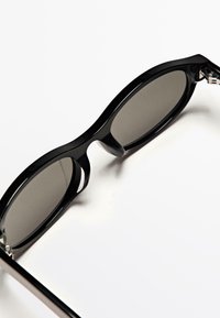 Occhiali da sole neri con montatura curva e lenti grigie, caratterizzati da una finitura lucida e dettagli laterali distinti.