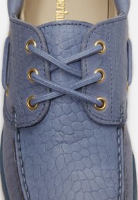 Μπλε πάνω μέρος παπουτσιού από υφή δέρματος με σταυρωτά κορδόνια ίδιου χρώματος περασμένα μέσα από έξι χρυσά οπές.