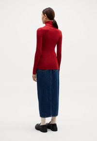 Rde prilegajoče se turtleneck majica v kombinaciji z dolgo jeans krilom. Majica ima rebrasto teksturo, medtem ko ima krilo klasičen modri denim videz.