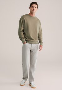 Olivno zelena majica sdugom rukavu s okruglim izrezom, uparena s laganim sivim hlačama ravnog kroja i svijetlim tenisicama s smešnim potplatom.