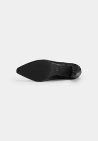 Zapato de tacón alto negro con punta afilada y superficie texturizada, con una suela lisa de goma y sin patrones de diseño visibles.