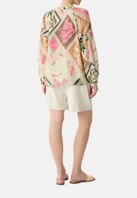 Lekka, wzorzysta bluzka z długim rękawem w pastelowych kolorach. Posiada kwiatowe wzory, geometryczne akcenty i luźny krój. Połączona z beżowymi szortami.