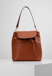 Borsa a secchiello in pelle marrone con finitura texture, chiusura con cordoncino e una singola tracolla regolabile. Presenta dettagli in metallo dorato.