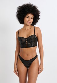 Schwarzes Lingerie-Set mit Pailletten, bestehend aus einem bauchfreien Oberteil mit vertikalen Streifen, dünnen Trägern und einem Ausschnitt vorne, kombiniert mit einem passenden Tanga.