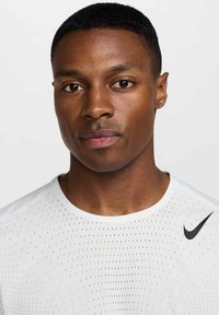 Ανδρική λευκή αθλητική μπλούζα με αεριζόμενο ύφασμα, στρογγυλή λαιμόκοψη και μαύρο λογότυπο Nike στον δεξιό ώμο. Λείο υλικό, κοντά μανίκια.