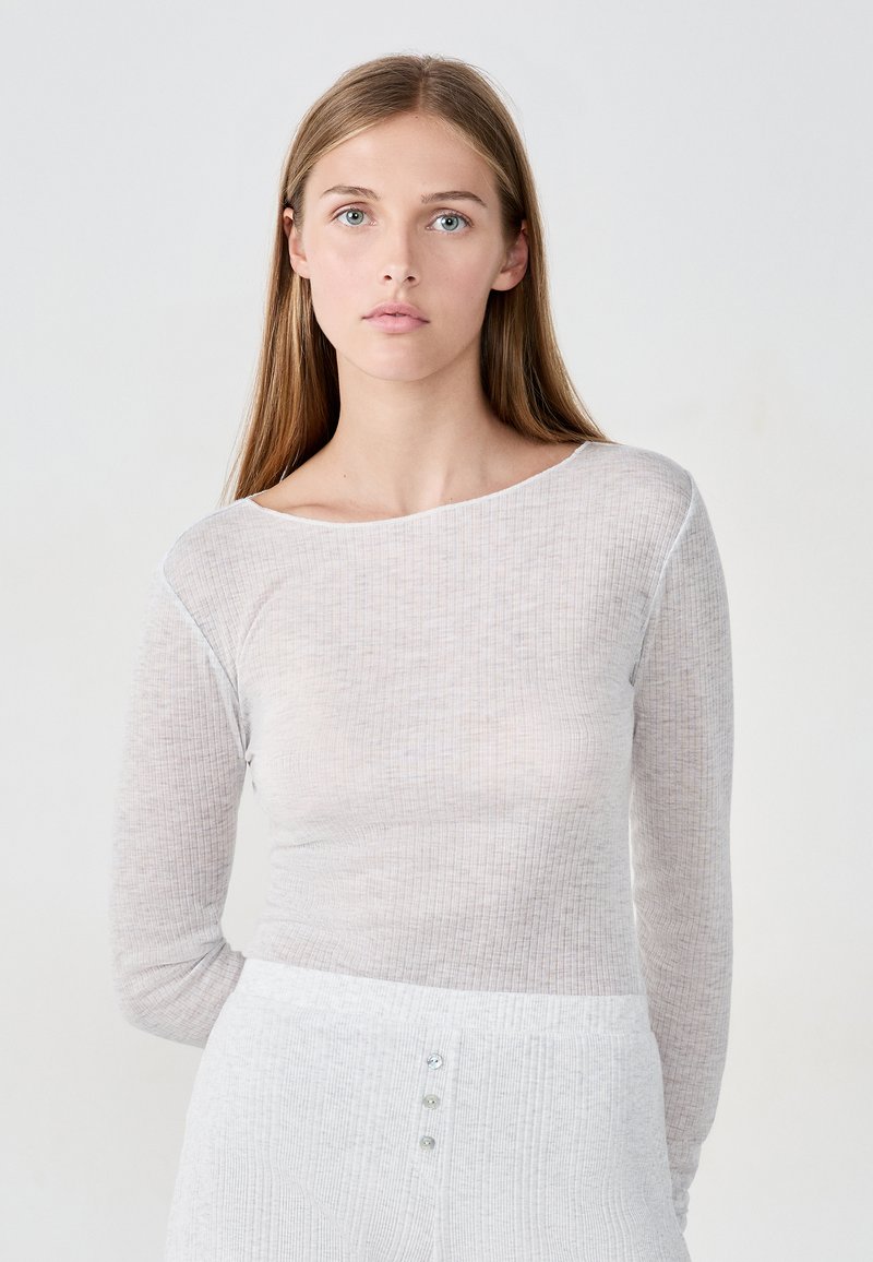 Jasnoszara bluzka z długim rękawem o prążkowanej fakturze, z szerokim dekoltem i subtelnymi pionowymi paskami; połączona z jasnoszarą spódnicą o teksturowanej powierzchni z guzikami.