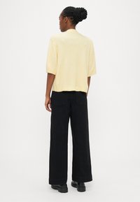 Short yellow knitted top with short sleeves, cropped cut, and a soft texture, paired with loose black pants and chunky black shoes.