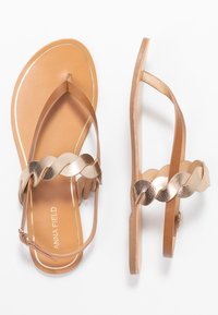 Flade sandaler med en glat tan sål og en metallisk guld fletrem, med et tærske-design og justerbar ankelspænde.